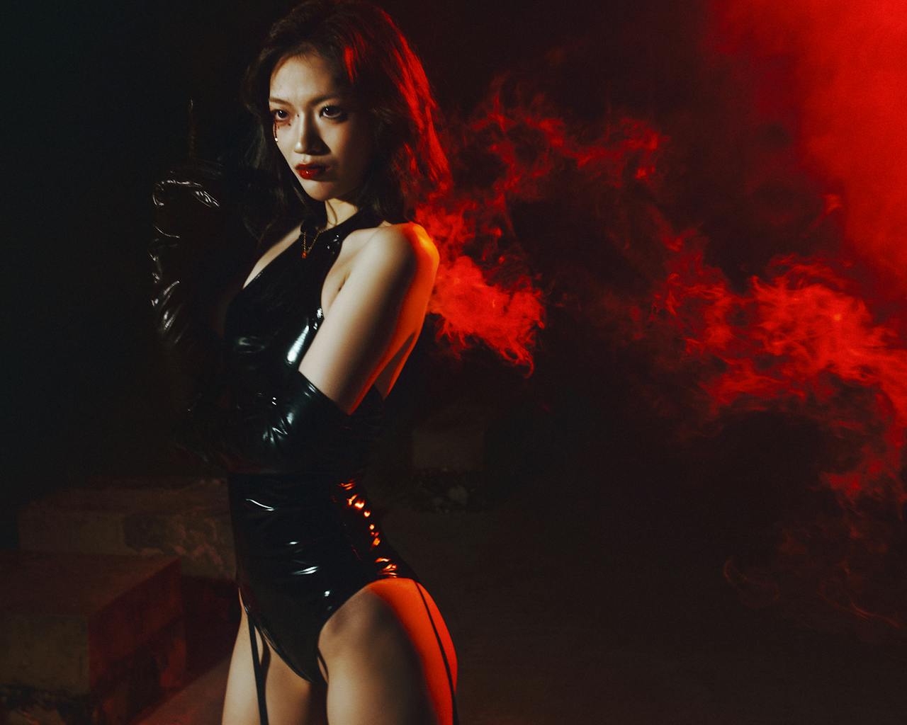 Woman in black latex outfit with red smoke, dramatic mood.